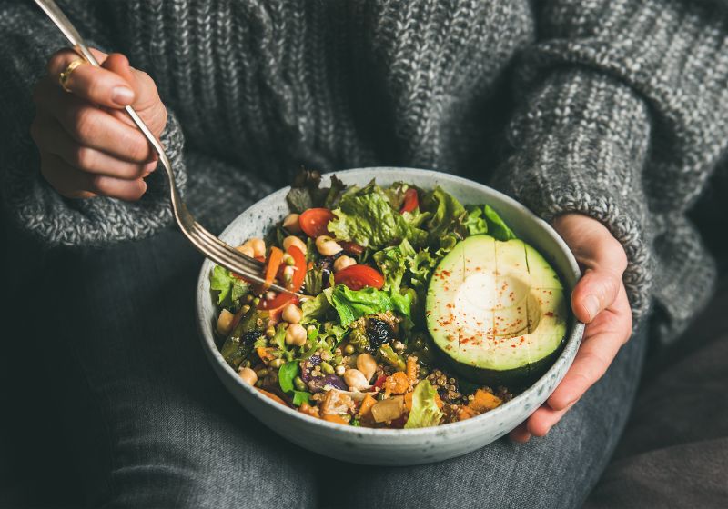 Schlaf und Ernährung: Bowl in Händen zeigt gesundes Essen wie Gemüse und Avocado