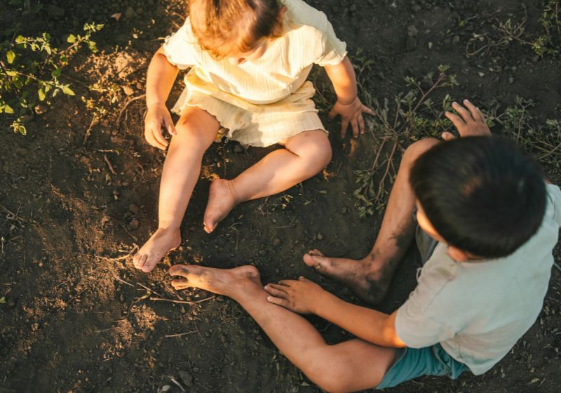 2 Kinder sitzen in der Erde und spielen im Dreck